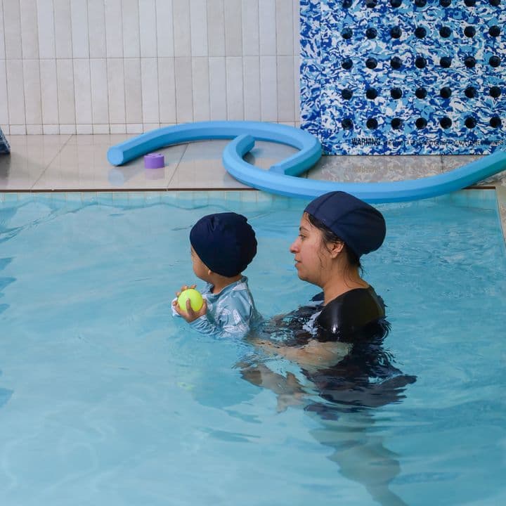 Una instructora en el agua con un bebé que sostiene una pelota