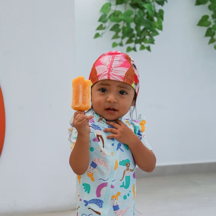 Una pequeña con gorro rojo y un helado, frente al muro de Nado