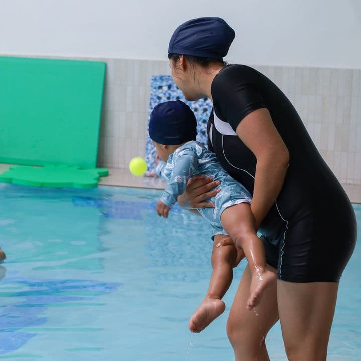 Una instructora carga a un bebé junto a la orilla